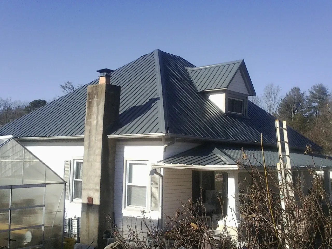 Dark blue standing seam metal roof on a white farmhouse with dormer — Slate & Tile Roof Repair by Roofing Brothers in East Taunton