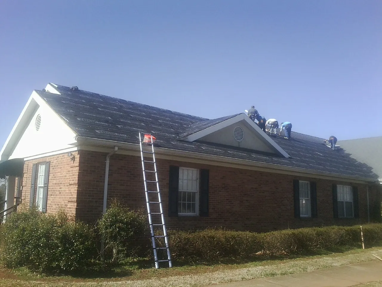 Crew tearing shingles off a brick ranch roof with a ladder set — Metal Roof Repair work by our crew in East Taunton