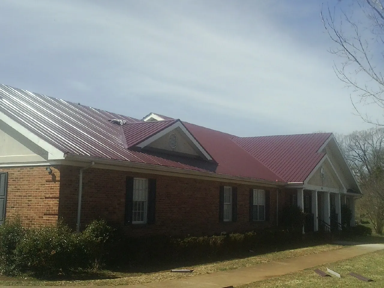 Red metal roof with gabled entries on a long brick building, from a Hail Damage Roof Repair job in East Taunton