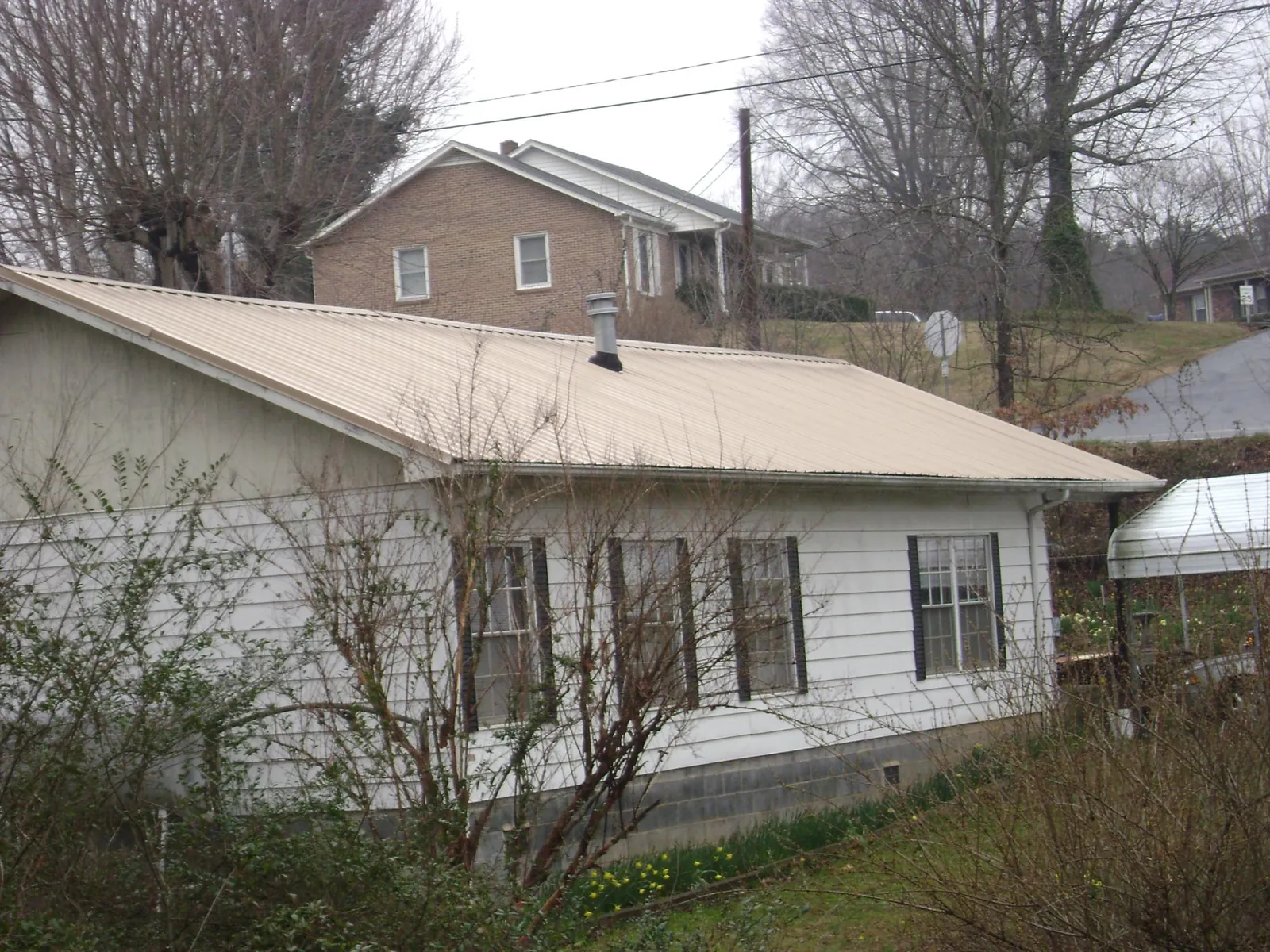 Tan metal roof on a white sided house set into a hillside — Commercial Roofing by Roofing Brothers in East Taunton